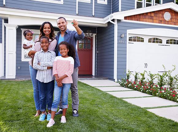 Family Smiling at Camera Standing in Front of a Blue Home with Home Insurance in Cary, Chapel Hill, Durham, Morrisville, Raleigh, Wake Forest