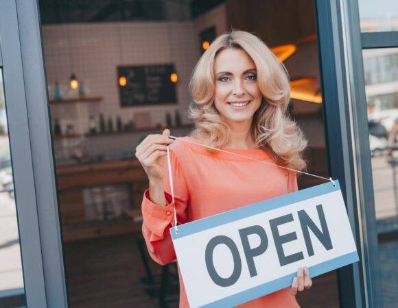 a woman holding an open sign with Small Business Insurance in Raleigh, Cary, Chapel Hill, Morrisville, NC, Wake Forest, Durham