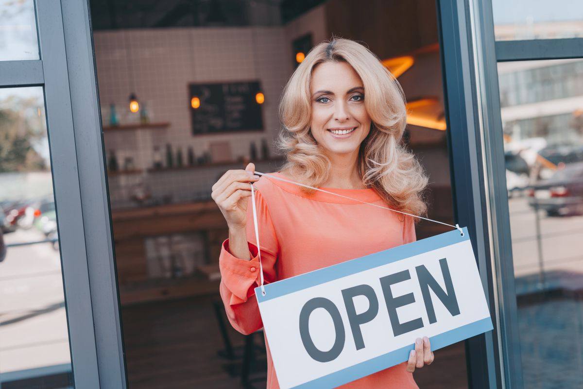 Business Owner Holding an Open Sign in Front of Her Store with Business Insurance in Durham, NC